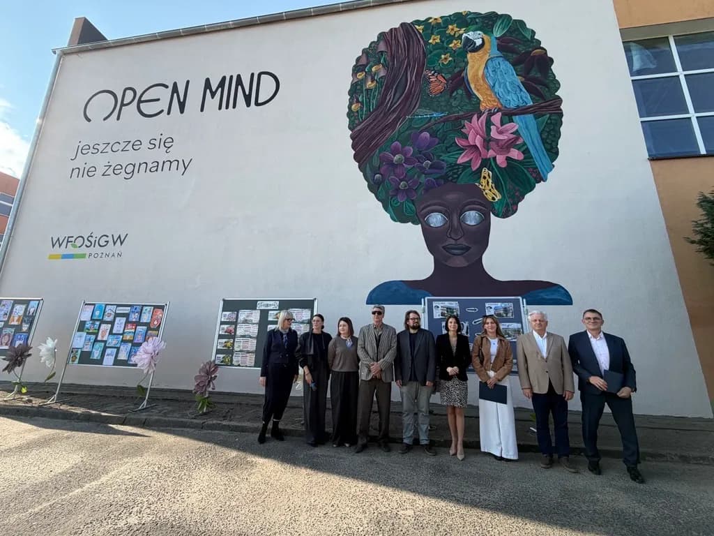 A group of people stand in front of a large outdoor mural that depicts a woman with her hair styled as a natural landscape, with text on the wall saying "OPEN MIND".