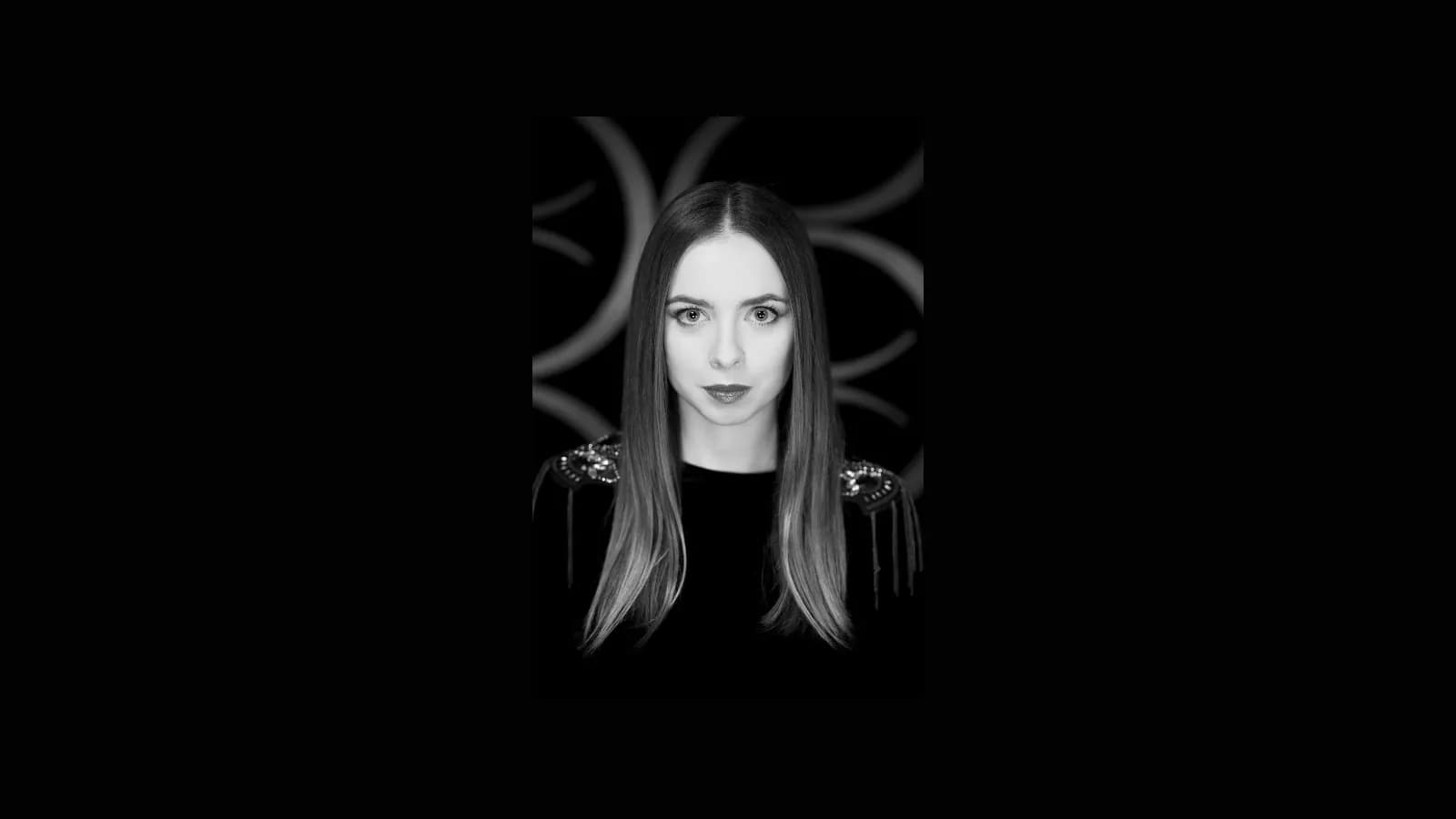A black and white portrait of a woman with long straight hair and a black top with embellished shoulders.