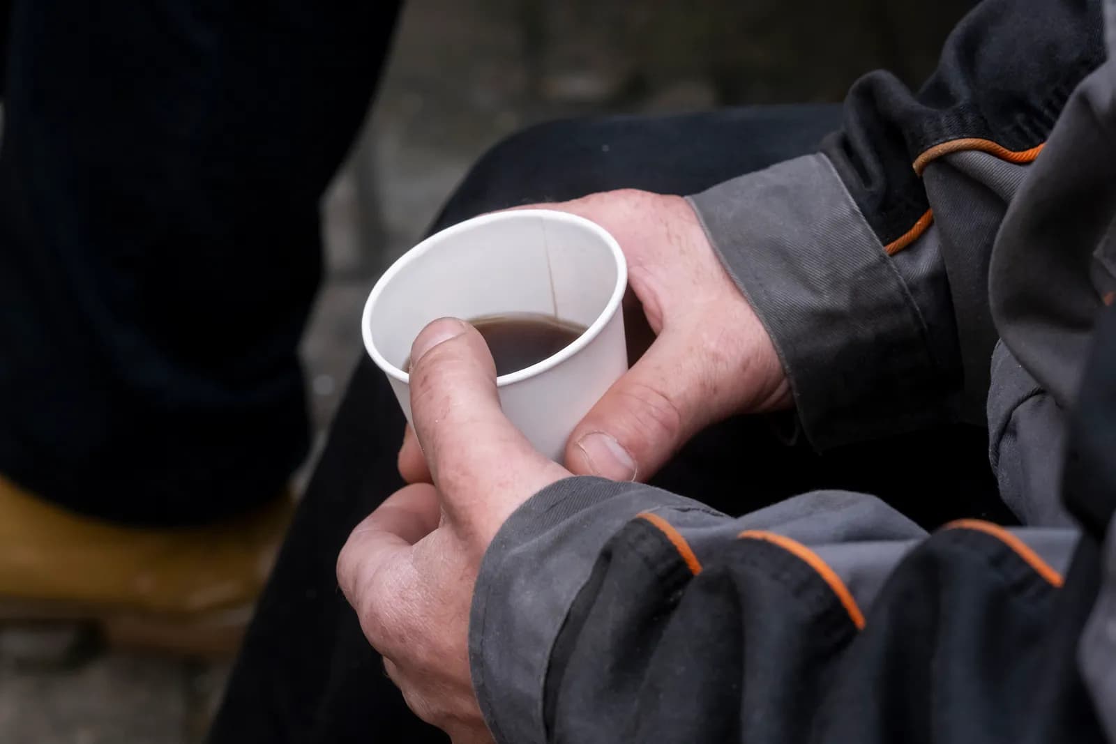 A person's hands cup a white paper cup filled with a dark liquid.